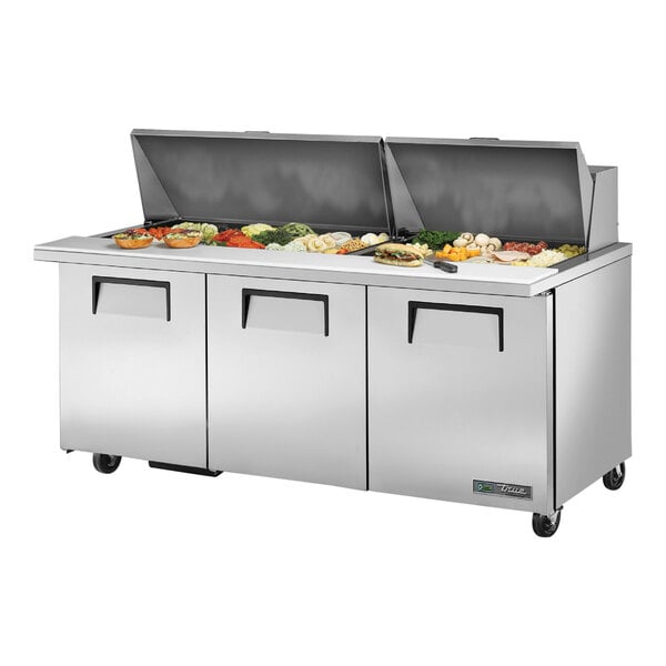 A True 3 door stainless steel refrigerated sandwich prep table with food on top.