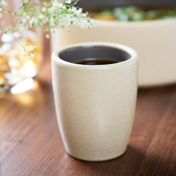 A Chef & Sommelier gray stoneware espresso cup filled with liquid on a table with a small white flower.