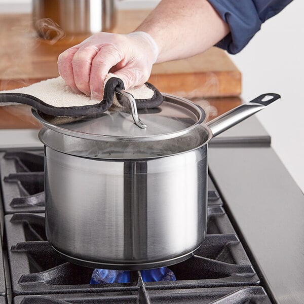 A person wearing gloves holding a Vigor stainless steel sauce pot over a stove.