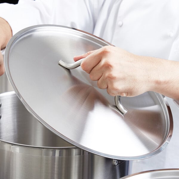 A chef holding a Vigor stainless steel lid for a pan.