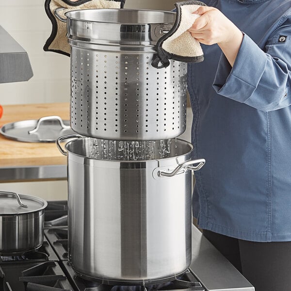 A person in a blue coat using a Vigor stainless steel pasta cooker.