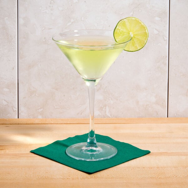 An Arcoroc martini glass with a green drink and a lime wedge on a napkin.