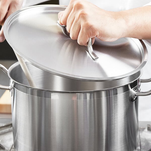 A hand holding a Vigor stainless steel lid over a pot.