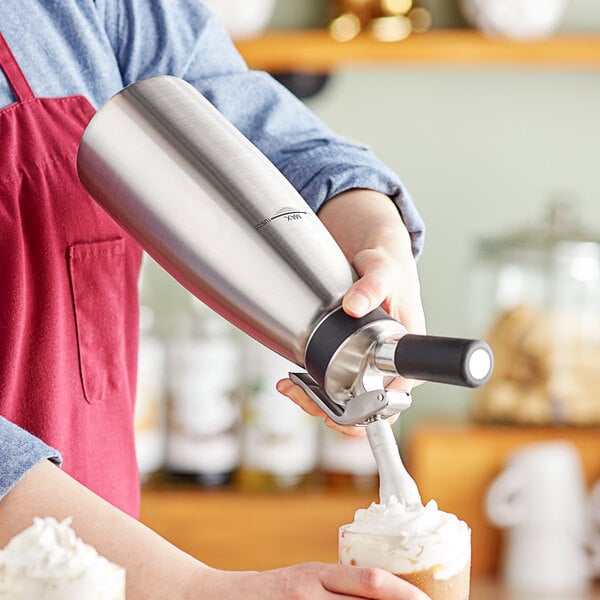 A person using an iSi whipped cream dispenser to add whipped cream to a drink.