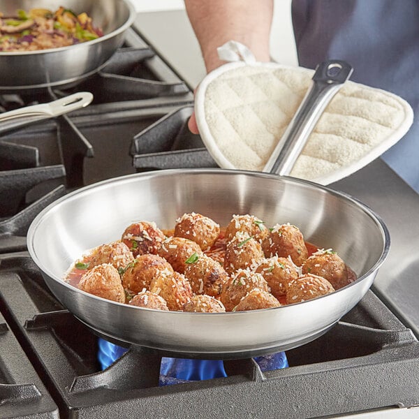A person cooking meatballs in a Vigor stainless steel fry pan on a stove.