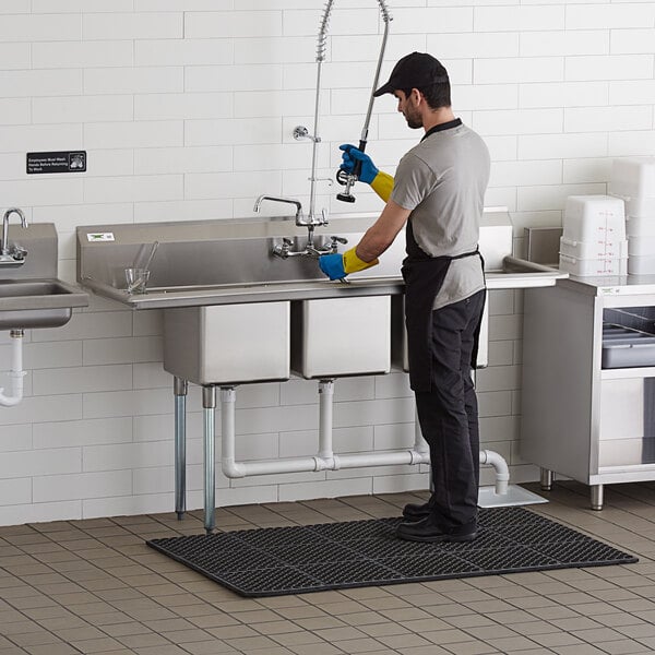 A man in gloves washing a Regency stainless steel three compartment sink.