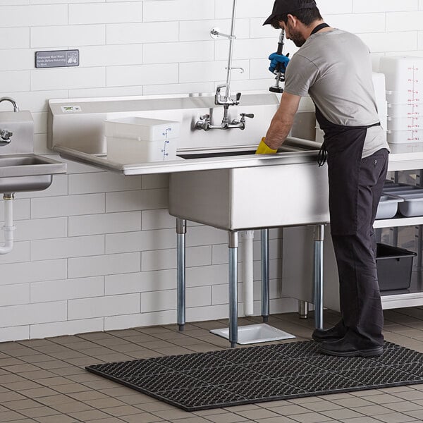 A man standing in a Regency stainless steel commercial sink in a professional kitchen.