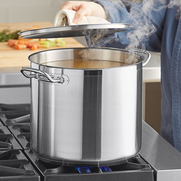 A person using a Vigor stainless steel stock pot to cook soup on a stove.