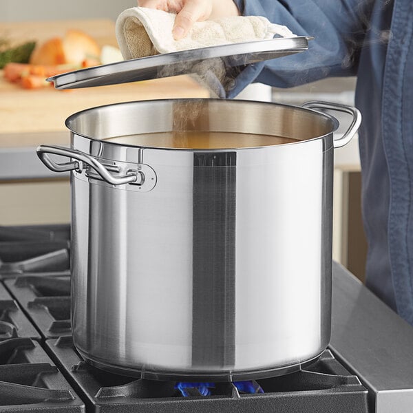 A person using a Vigor stainless steel stock pot to cook soup on the stove.