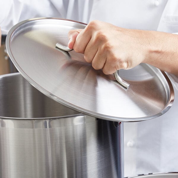 A hand holding a Vigor stainless steel lid over a pot.