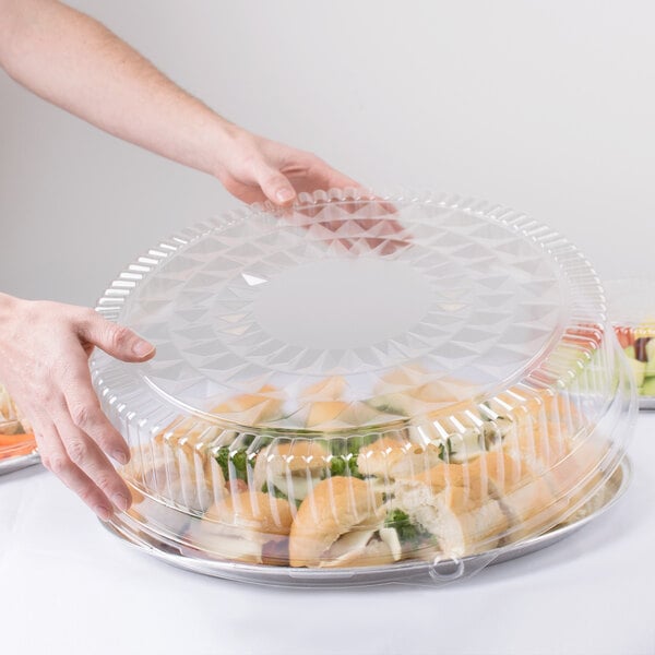 A person holding a Durable Packaging clear plastic round high dome lid over a container of food.