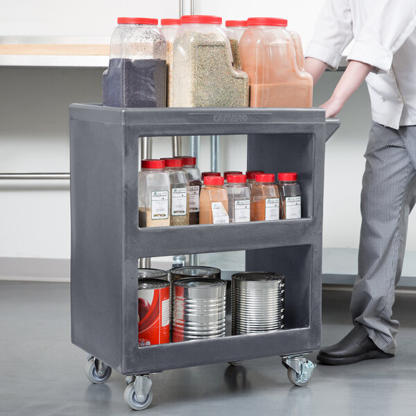 A man pushing a Granite Gray Cambro service cart with food containers.