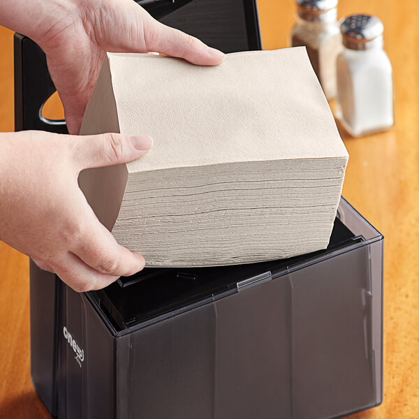 A person holding a stack of OneUp by Choice Kraft wide interfold dispenser napkins.