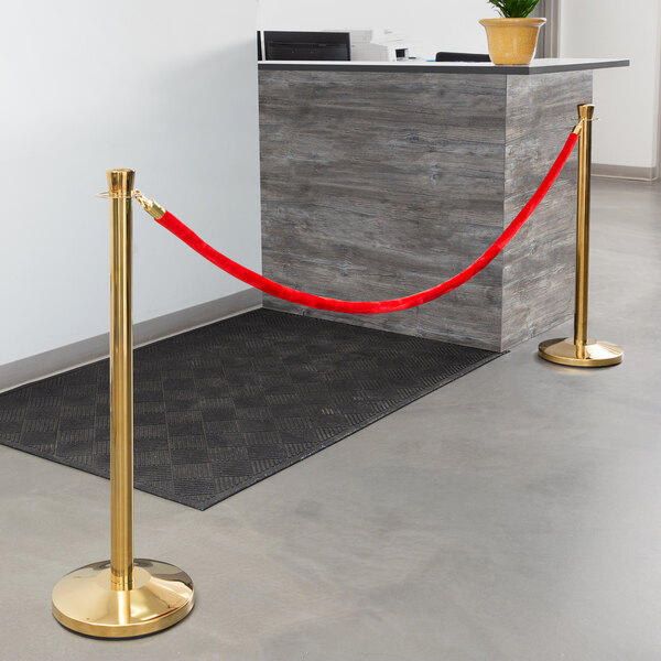 A Lancaster Table & Seating gold rope crowd control barrier set with a red rope in use in front of a reception desk.