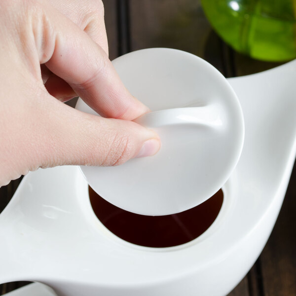 A person pouring liquid into a white teapot.