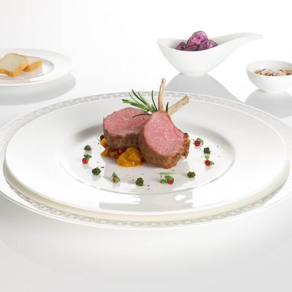 A Villeroy & Boch white bone porcelain flat plate with a piece of meat and vegetables on it.