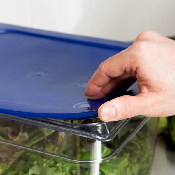A hand using a Carlisle blue plastic lid to cover a food container of lettuce.