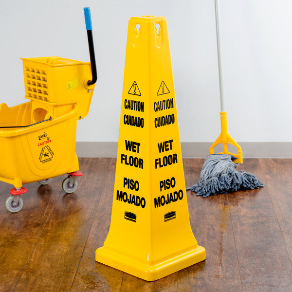 A Rubbermaid yellow caution wet floor cone in a room with a mop and bucket.
