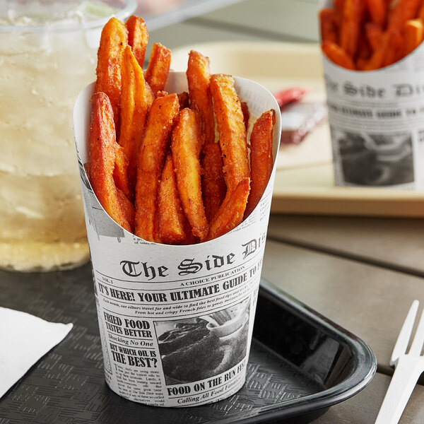 A Choice paper scoop cup with a newsprint design filled with french fries on a table.