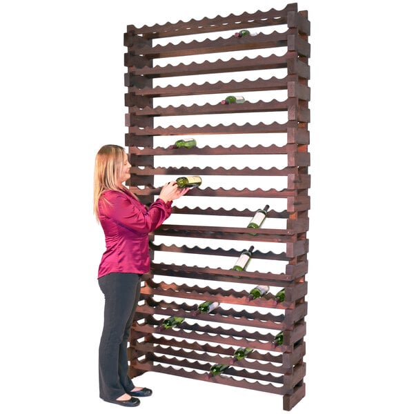 A woman standing next to a Franmara stained wooden wall mount wine rack filled with wine bottles.