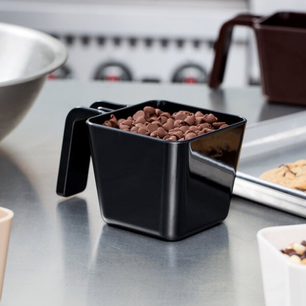 A black container with a Carlisle portion scoop full of chocolate chips.