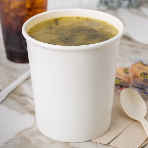 A white Choice paper cup filled with soup on a table with a spoon.