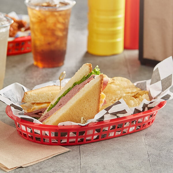 A red oval plastic fast food basket with a sandwich, chips, and a drink on a table.