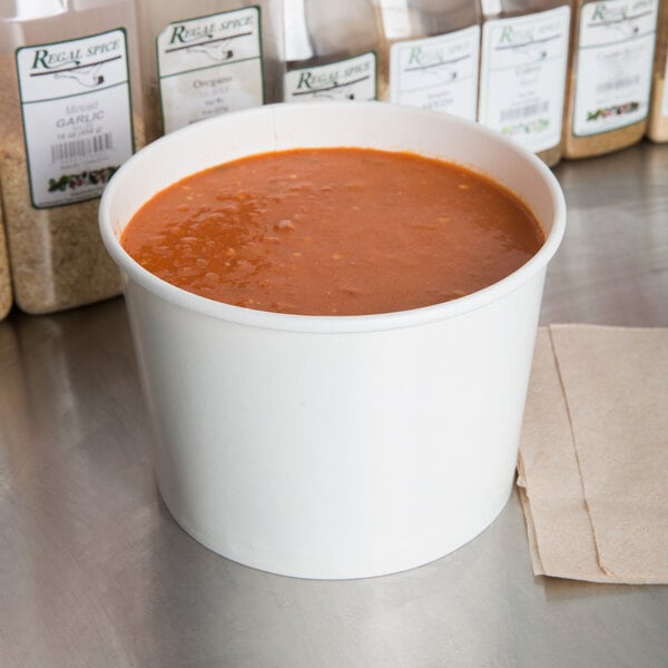 A white paper food bowl filled with tomato soup on a counter.