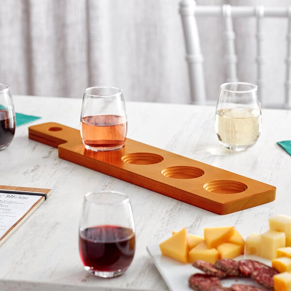 An Acopa walnut flight paddle holding wine and cheese glasses on a table.