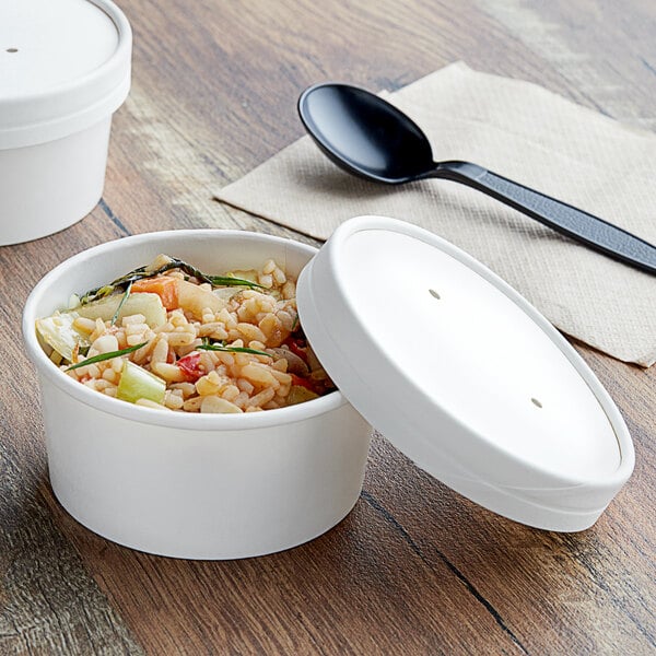 A table with a white Choice paper food container and lid filled with food.