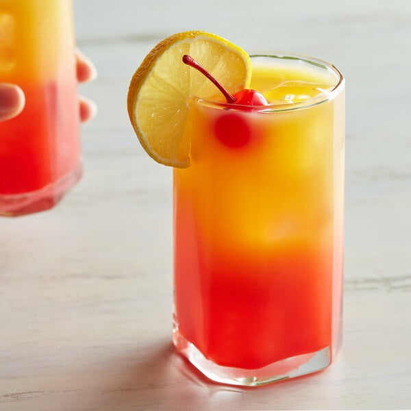 A hand holding a glass of orange and red liquid with a cherry and a slice of lemon.
