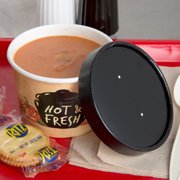 A tray with a bowl of soup and crackers with a black and white dotted lid.