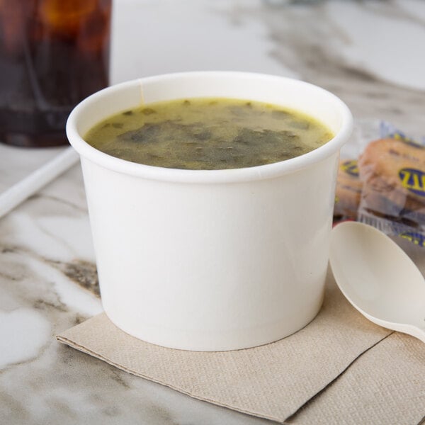 A white double poly-coated paper food cup filled with soup with a spoon.
