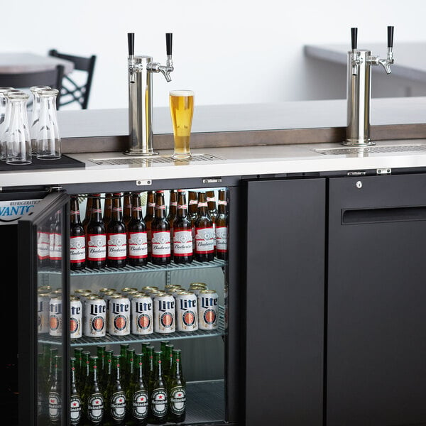 An Avantco black kegerator with beer bottles and glasses on top.