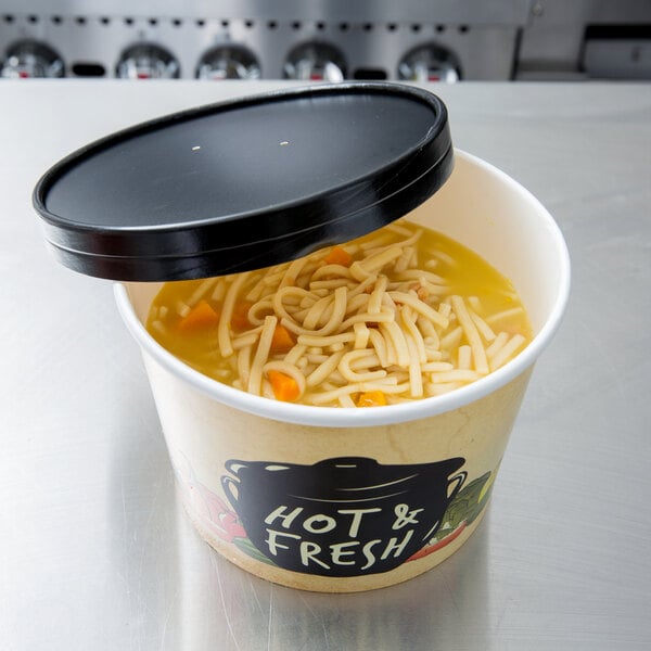 A white Choice paper soup bowl filled with noodles and carrots with a black vented paper lid.