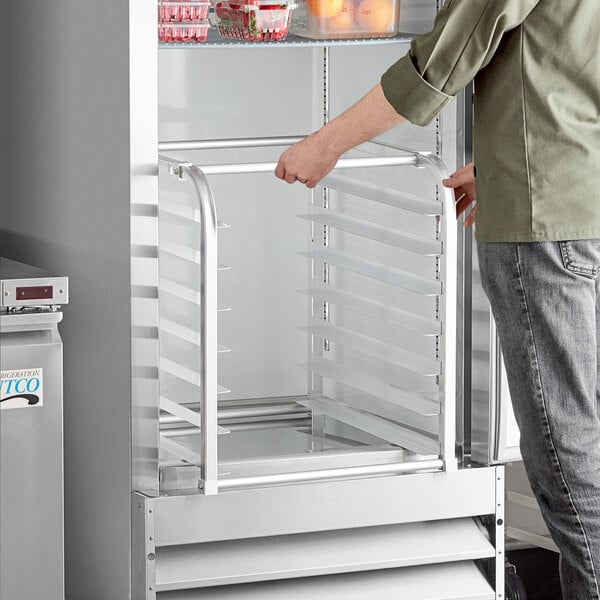 A person opening a refrigerator with a Regency aluminum sheet pan rack inside.