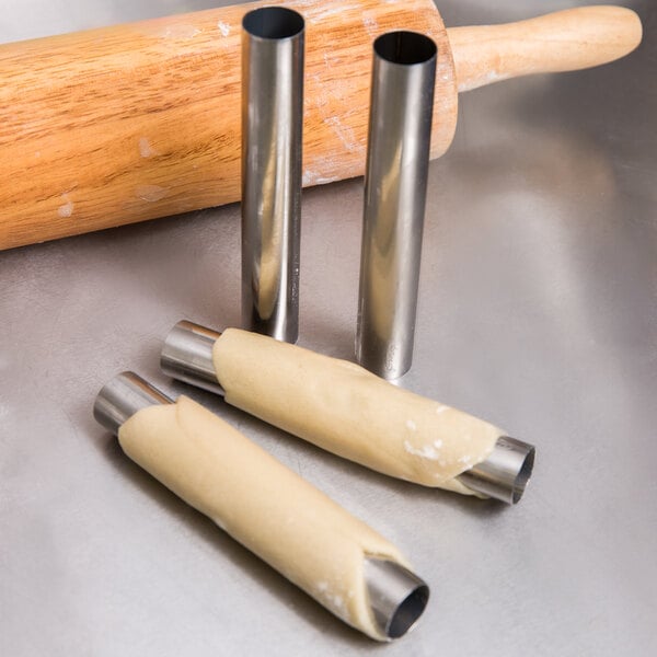 A close-up of Ateco stainless steel cannoli forms being used to roll dough.