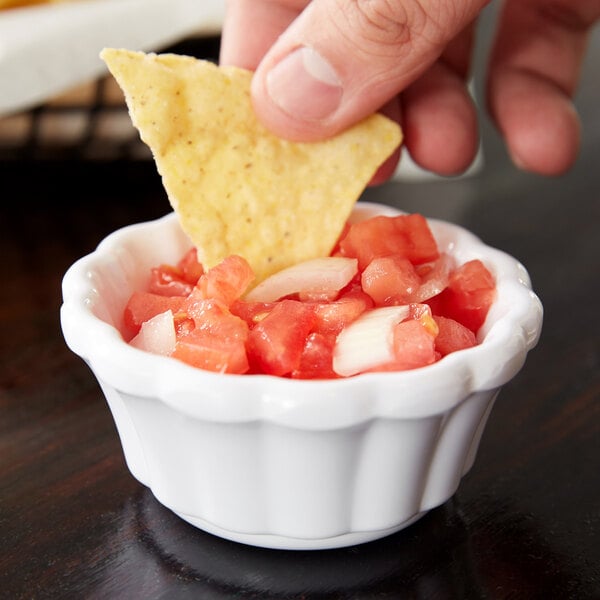 A person holding a chip dips it into a bowl of salsa.