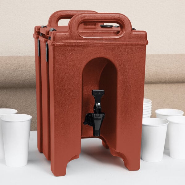 A red plastic Cambro insulated beverage dispenser with a black spigot on a white table.