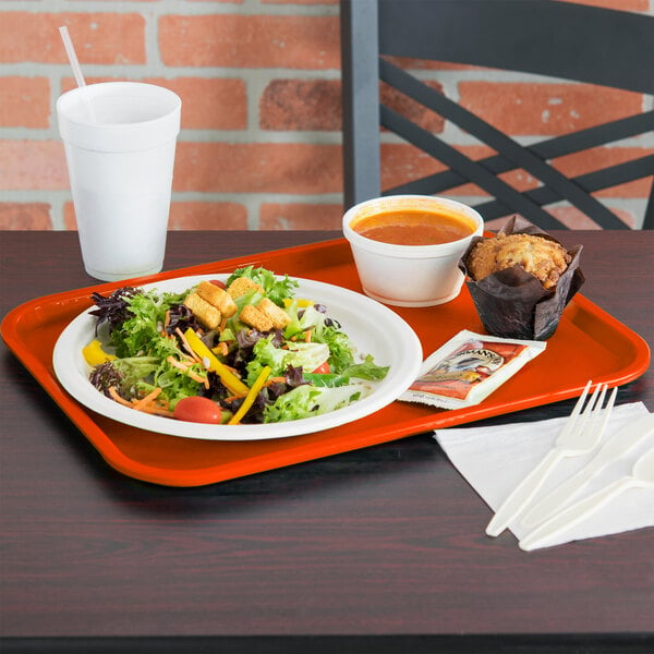 An orange Vollrath fast food tray with a plate of salad and a muffin on it.