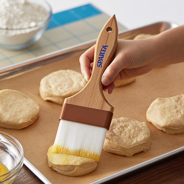 A person using a Carlisle Sparta Spectrum pastry brush to paint biscuits on a tray.