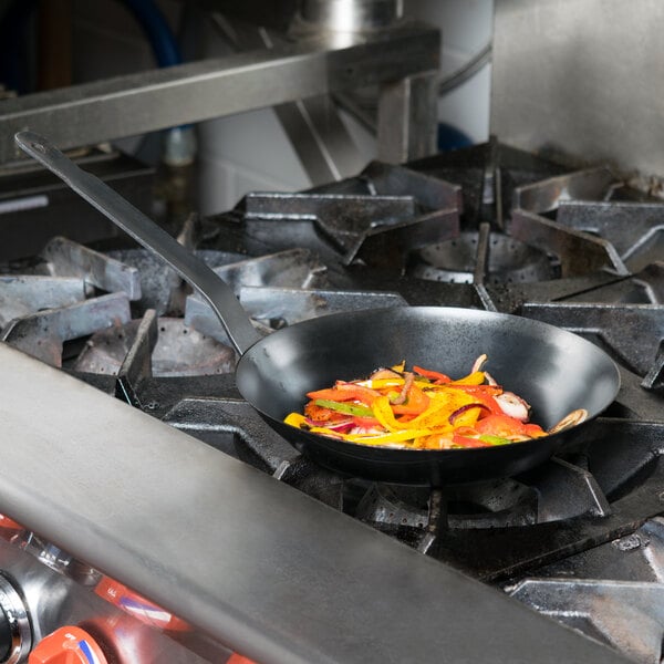 A Town French style carbon steel fry pan filled with vegetables cooking on a stove.