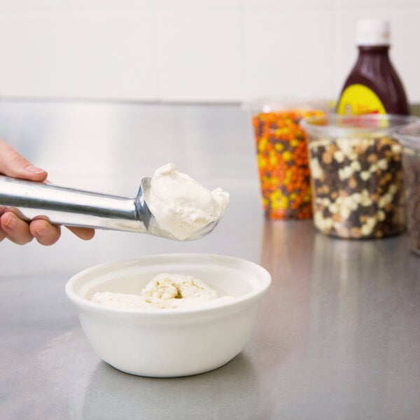 A person using a Zeroll aluminum ice cream scoop to put ice cream in a bowl.