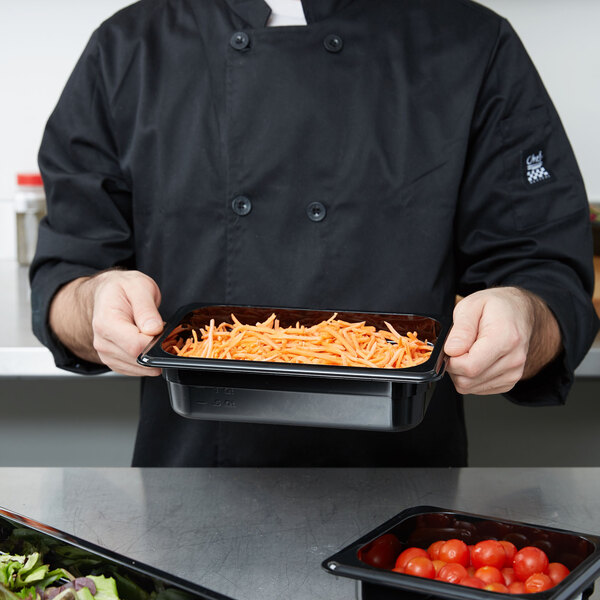 A chef holding a Cambro black plastic food pan filled with food.
