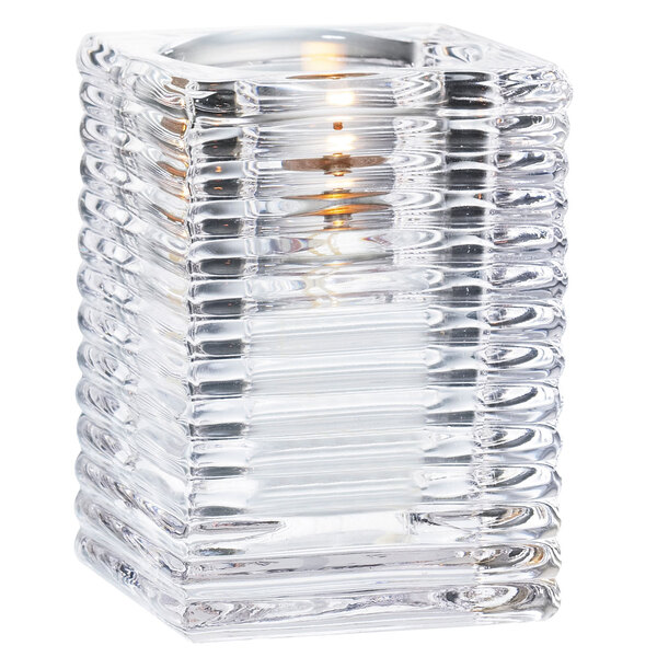 A Sterno clear glass candle holder with a lit candle inside.