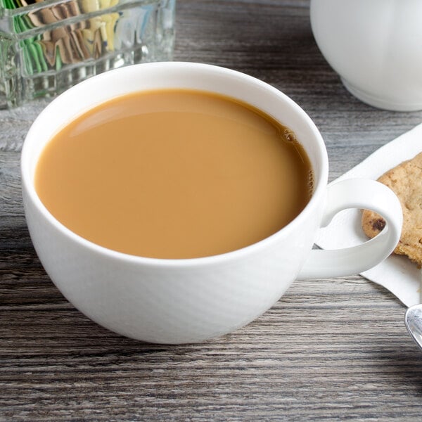 A white Villeroy & Boch porcelain cup filled with coffee with a cookie on the saucer