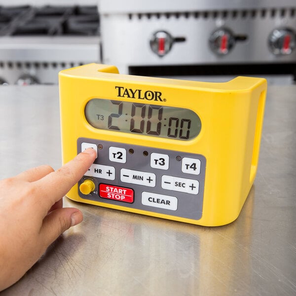 A hand pressing a yellow button on a Taylor digital kitchen timer.