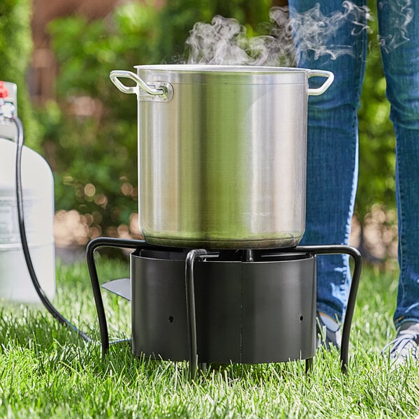 A person standing next to a Backyard Pro outdoor stove with a large metal pot on the burner.