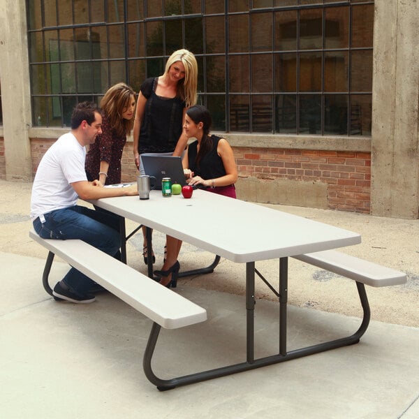 A group of people sitting at a Lifetime rectangular plastic picnic table.