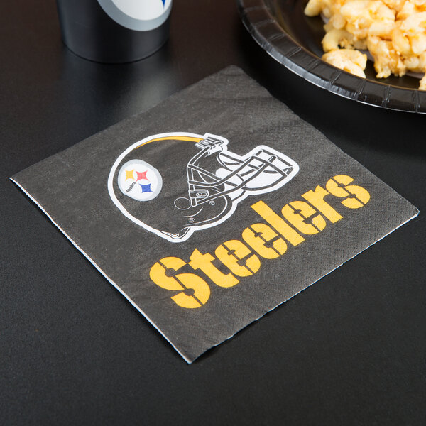 A Creative Converting Pittsburgh Steelers luncheon napkin with a helmet on it next to a plate of food.